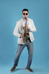 Fototapeta na wymiar Young man playing saxophone on light blue background