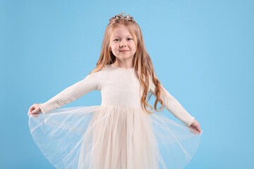 Fototapeta na wymiar Cute girl in beautiful dress with diadem on light blue background. Little princess