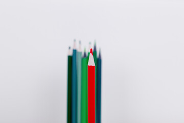 a red pencil in the foreground as a leader. a few pencils in the background like a crowd. wooden colored pencils on a white background
