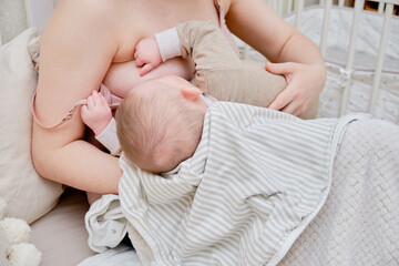 Woman mother breastfeeds infant baby boy sitting on home bed. Mom feeds milk toddler child in the bedroom