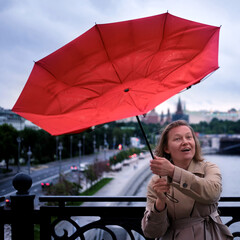 Smiling woman with red umbrella during strong wind and stormy weather