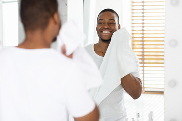 Daily Hygiene. Handsome Black Man Wiping Face With Towel In Bathroom