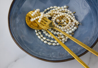 Creative layout with dark blue plate, golden fork, spoon ans spaghetti pearls on white background....
