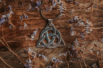 Fototapeta na wymiar silver triquetra pendant on a wooden table in dry flowers