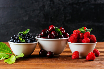 a variety of wild berries in a bowl on a wooden background. rasp