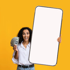 Cashback concept. Shocked woman holding huge smartphone with blank screen and cash money dollar...