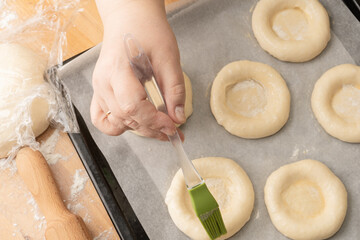 Female hand smears the dough culinary brush. baking at home, ring of dough with quark in the middle.  Ball dough with cottage cheese - Powered by Adobe