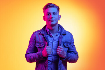Closeup young handsome man wearing casual youth style clothes isolated on orange background in neon light, filter. Concept of emotions, beauty, fashion