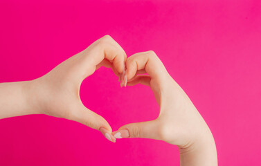 Fototapeta premium female hands making heart gesture on pink background