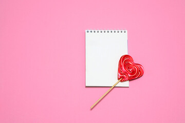 on a bright pink background a red lollipop in the shape of a heart, a sheet for notes. card, congratulations on Valentine's Day. romantic background. place for text