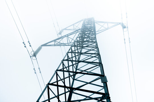View of a high voltage electrical tower. The top of the tower is blurred by fog. Electric power is becoming scarcer and more expensive.