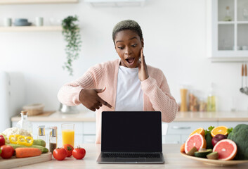 Shocked millennial african american lady with open mouth point finger at laptop with blank screen