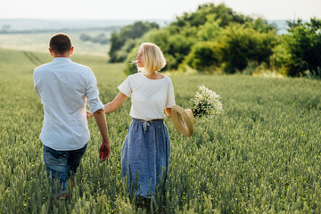 Summer Lifestyle. Rear view shot of woman walking with her boyfriend on wheat field. Couple enjoying a walk through wheat land.