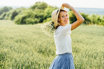 Obraz premium Summer Lifestyle Concept. Trendy adult woman in stylish summer dress feeling free in the field with wild flowers in sunshine.