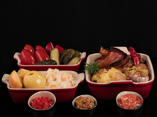 Baked pork knuckle with potatoes, cabbage, pickles, and sauce. On a black background.