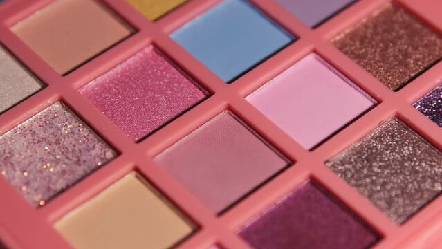 Make up eyeshadow multicolor palette illuminated by light and immersed in darkness. Colorful bright eye shadows set for visage. Rotation cosmetic background.
