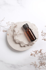 Cosmetic serum in glass bottle on stone podium. Natural cosmetic product packaging design, branding. Marble background with flower branch.