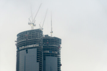 Skyscraper construction on a foggy day. Construction cranes are hidden in the fog. Unfinished high-rise building. Building glazing.