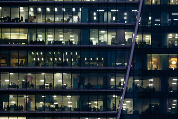 Workers in a box. Office building light at night. A skyscraper made of glass and metal lighr up in the evening. Windows of Skyscraper Business Office.