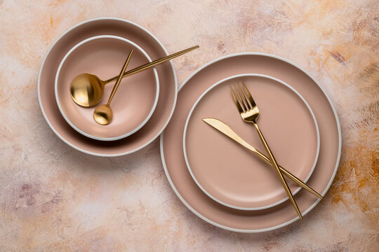 Collection of round beige plates of different sizes on the table, top view. Golden cutlery and crockery for serving and eating. Modern craft ceramic tableware, trendy tableware.