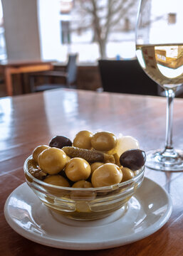 Plate of green olives, black olives, gherkins and spring onions. View of the dish with a glass of white wine
