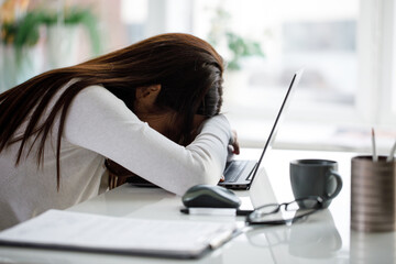 A young business woman is sitting at a table with a laptop and sleeping. The concept of overtime and overwork.