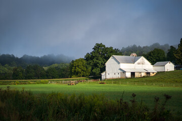 Fototapeta na wymiar White Barn and Green Fields Underneath a Rainy Sky