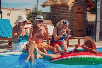 Senior people eating watermelon and sunbathing by the swimming pool