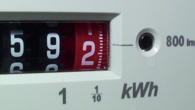 Macro close-up of a household electric meter showing the red dial number moving, kWh symbol. Concept for energy, higher bills, price rise, meter reading, cost of living and electricity supplier. 