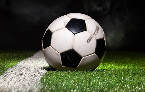Low angle view of soccer ball on grass field with dark background and smoke