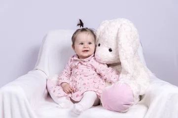 Fotobehang süß lächendes Baby sitzt mit weißem Stoffhasen auf weißem Sessel © Ingeborg Zeh