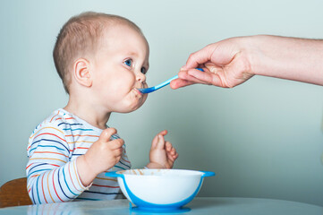 Parent feeds child from spoon close-up. Handsome toddler sitting with plate close-up. Baby...