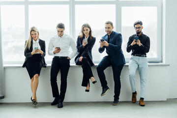 Conceptual multi ethnic young people sit in queue holding electronic devices using internet while waiting job interview. Generation addicted with modern devices, employment, human resources