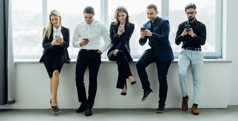 Group of business people using mobile phones and sitting on couch. Networking and teamwork. Working on project with wireless technology and data. Happy friends texting with smartphones.