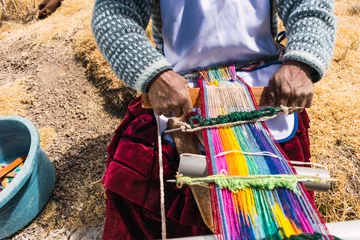 Foto op Canvas poor indigenous adult woman artisan with blue mask and typical ancestral costume weaving in times of covid-19 pandemic on a sunny day in the Andes mountain range © roy