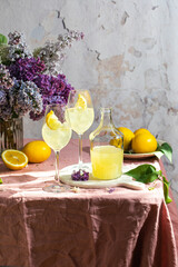 A bottle of Italian traditional liqueur limoncello with glasses, lemons and a vase with blooming...
