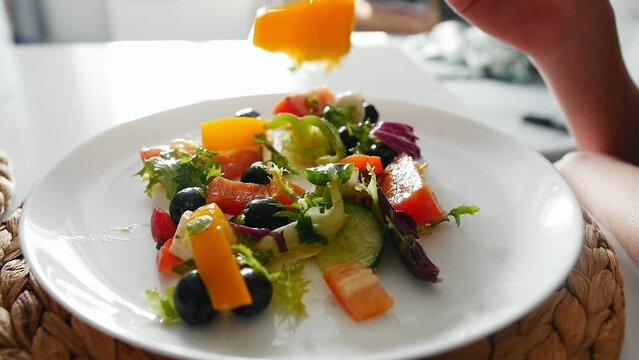A girl eats vegetable salad with a fork from a white plate