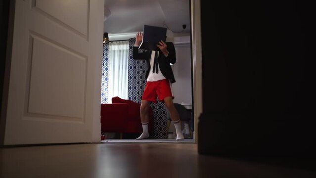 Cheerful businessman in red shorts and blazer dancing at home with a laptop computer
