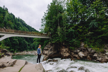 Happy male tourist standing outdoors in the forest near the mountain river.