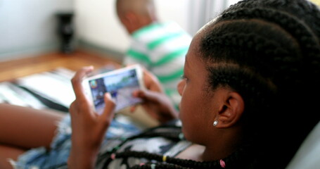 Teen black girl playing game on phone at home couch. African teenager using smartphone