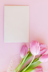 Empty greeting card and pink tulips bouquet on pink background flat lay. Greeting card template with space for text. Happy womens day. 8 march. Happy Mothers day