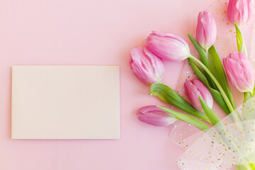 Empty greeting card and pink tulips bouquet on pink background flat lay. Happy womens day. 8 march. Happy Mothers day Greeting card template with space for text