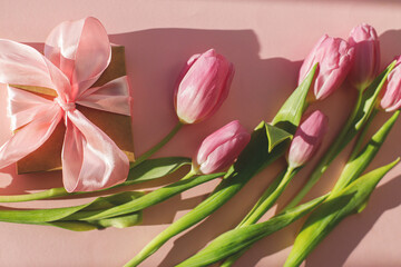 Pink tulips and gift box in sunlight on pink background. Modern creative spring banner. Happy womens day. Hello spring. Happy Mothers day. Floral Greeting card. 8 march