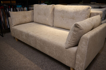 Exhibition of soft furnishing in the furniture store showroom. Stylish minimalist beige sofa with cushions in the showroom of a furniture store. Home design and decoration concept