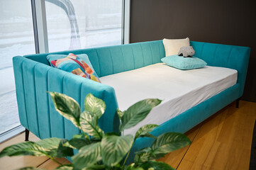 Modern stylish and minimalist children's sofa bed with soft bright turquoise velour fabric, on display for sale in the showroom of the highest quality furniture store