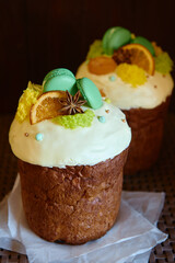 Glazed easter cake decorated with macaroons, dried orange slice and candies on dark background, copy space. Happy Easter holidays. Kulich