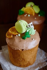 Glazed easter cake decorated with macaroons, dried orange slice and candies on dark background, copy space. Happy Easter holidays. Kulich
