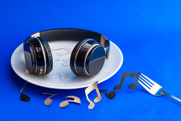 black headphones on a white plate and electric blue background ready for consumption