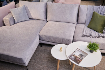 High angle view of a stylish comfortable sofa upholstered with light velour fabric with colorful pillows and a small journal table on display in the furniture store showroom