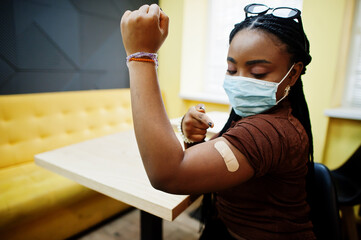 Stay safe! Black woman, wearing mask, showing vaccinated arm after vaccine injection.